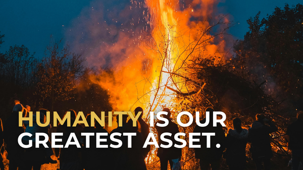 People standing around a bonfire, with sparks floating high into the sky. Text overlay says "Humanity is our greatest asset."